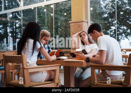 Assis dans un café et avoir une conversation. Quatre jeunes étudiants dans les tenues ont rencontre à jour de pluie Banque D'Images