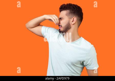 Mauvaise odeur. Vue latérale du malheureux homme confus brunette avec barbe en blanc T-shirt apnée avec les doigts sur le nez, de se détourner de l'odeur fétide, Banque D'Images