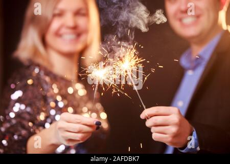 Photo de l'heureux couple avec verres de champagne et cierges sur fond noir en studio Banque D'Images