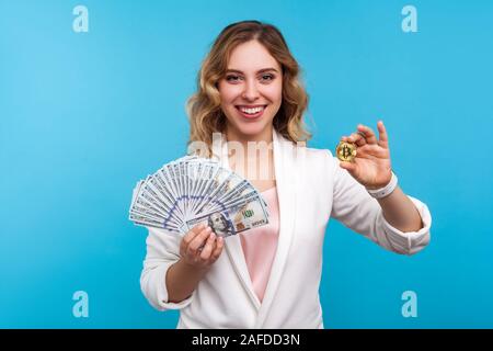 Cryptocurrency. Portrait de heureux charmante femme avec les cheveux ondulés en veste blanche holding golden physique et bitcoin, dollars de publicité btc crypto Banque D'Images