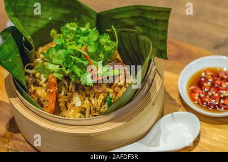 Char kway teow frit nouilles de riz de persil plat sur le dessus et servi dans des feuilles de banane dans un panier de bambou Banque D'Images