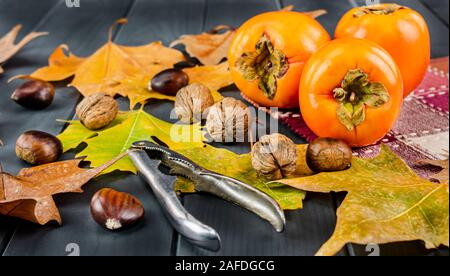 Le kaki avec les feuilles d'automne et des fruits tels que les châtaignes, noisettes, noix et amandes, avec un ouvreur sur planche en bois gris Banque D'Images