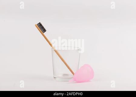 Brosse à dents en bambou et coupelle menstruelle en verre sur fond blanc. Concept zéro déchets Banque D'Images