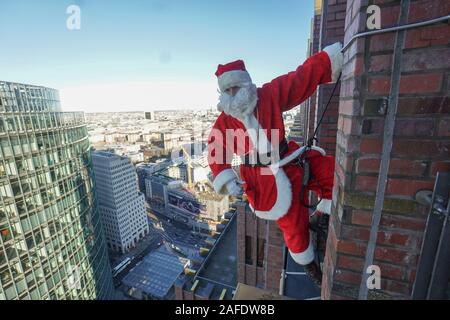 Berlin, Allemagne. Le 15 décembre, 2019. Santa Claus est suspendu à la façade du panorama point sur la Potsdamer Platz au cours d'une action d'escalade à grande hauteur. Credit : Jörg Carstensen/dpa/Alamy Live News Banque D'Images