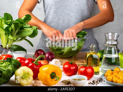 Femme prépare salade de laitue romaine, salade de cuisson dans un bol en verre dans la cuisine. Régime alimentaire sain concept. Banque D'Images