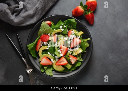 Salade de fraises d'été avec épinards, fromage feta, avocat, vinaigre balsamique et huile d'olive dans une assiette. Nourriture végétalienne. Concept d'alimentation saine Banque D'Images