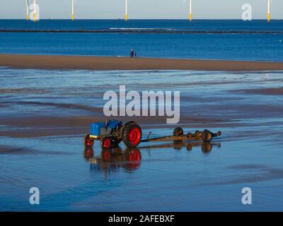 Un tracteur et remorque fishermans stationnée sur la plage de Redcar pour transporter son bateau de la mer après la pêche et le parc éolien de Redcar derrière Banque D'Images