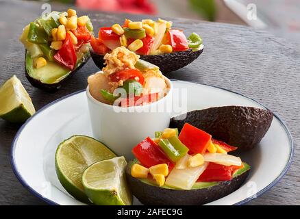 Vue avant d'Avocats farcis aux légumes, des portions de lime frais et un petit bol avec des œufs brouillés, pommes de terre et les légumes, sur une assiette blanche Banque D'Images