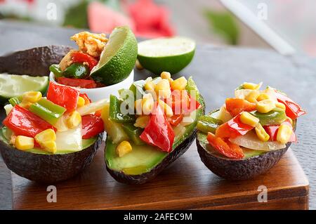 Vue de face de plusieurs avocats farcis aux légumes sur une planche en bois, des portions de lime frais et un petit bol avec des œufs brouillés, pommes de terre et de ve Banque D'Images