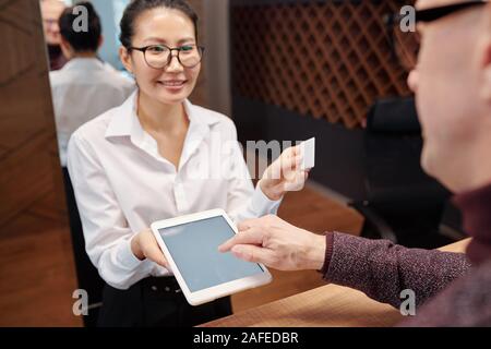 Main de mature businessman sur tablet display et jeune réceptionniste avec carte Banque D'Images