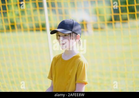 Portrait d'un garçon d'âge scolaire dans une casquette de baseball dans le contexte d'un filet de but de football Banque D'Images