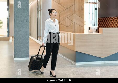 Young Asian businesswoman pulling suitcase en attendant de voir l'annonce Banque D'Images