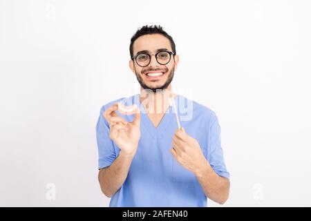 Dentiste contemporain uniforme bleu en vous montrant de fausses dents et brosse à dents Banque D'Images