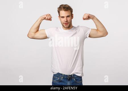 Sassy et confiant masculin barbu blond caucasian man, du fond blanc avec flexion des biceps, être en forme, d'entraînement et de se vanter, d'être Banque D'Images