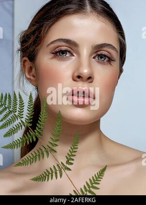 Portrait d'un adulte femme brune sur un fond blanc avec des soins de la peau, fougère vert concept, une belle peau et des mains avec manucure ongle. Banque D'Images