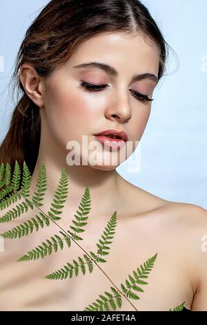 Portrait d'un adulte femme brune sur un fond blanc avec des soins de la peau, fougère vert concept, une belle peau et des mains avec manucure ongle. Banque D'Images