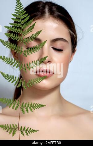 Portrait d'un adulte femme brune sur un fond blanc avec des soins de la peau, fougère vert concept, une belle peau et des mains avec manucure ongle. Banque D'Images