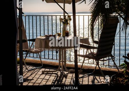 Petit-déjeuner servi une table pour deux avec deux chaises et parasol voyage derrière les balustrades métalliques sur la plage du lac de Garde à la fin de l'aube. La Lombardie, ita Banque D'Images