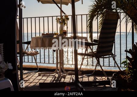 Petit-déjeuner servi une table pour deux avec deux chaises et parasol voyage derrière les balustrades métalliques sur la plage du lac de Garde à la fin de l'aube. La Lombardie, ita Banque D'Images