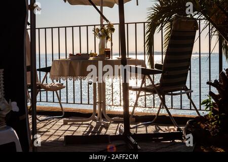 Petit-déjeuner servi une table pour deux avec deux chaises et parasol voyage derrière les balustrades métalliques sur la plage du lac de Garde à la fin de l'aube. La Lombardie, ita Banque D'Images