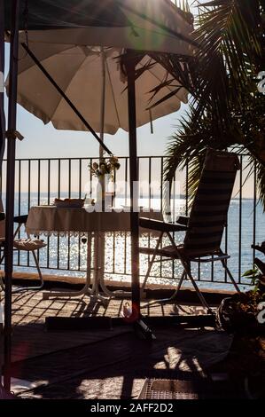 Petit-déjeuner servi une table pour deux avec deux chaises et parasol voyage derrière les balustrades métalliques sur la plage du lac de Garde à la fin de l'aube. La Lombardie, ita Banque D'Images