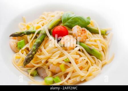 Nouilles aux crevettes et asperges à la sauce aux herbes sur une assiette blanche décorée avec des feuilles de basilic et de tomate Banque D'Images