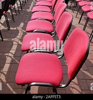 Des rangées de chaises de bureau à vide saturé couleur cramoisi sièges sont situés sur la chaussée à l'extérieur par beau temps d'été festival pendant Banque D'Images