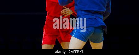 Deux hommes en bleu et rouge sambo wrestling wrestling jaune sur un tapis dans la salle de sport Banque D'Images
