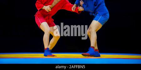 Deux hommes en bleu et rouge sambo wrestling wrestling jaune sur un tapis dans la salle de sport Banque D'Images