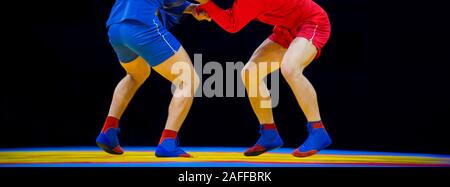 Deux hommes en bleu et rouge sambo wrestling wrestling jaune sur un tapis dans la salle de sport Banque D'Images