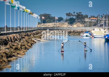 Deux femmes manoeuvrer leur stand up paddle boards dans un canal près de la jetée et du port de plaisance de chemin dans le port de Santa Barbara, Santa Barbara, CA, Banque D'Images