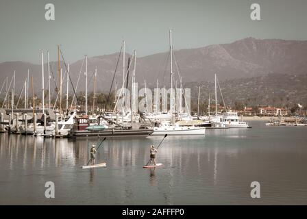 Deux femmes leur meilleur manœuvrier stand up paddle boards dans un canal près de voiliers et yachts amarrés dans la marina dans le port de Santa Barbara, Santa Banque D'Images