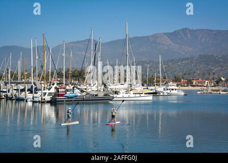 Deux femmes leur meilleur manœuvrier stand up paddle boards dans un canal près de voiliers et yachts amarrés dans la marina dans le port de Santa Barbara, Santa Banque D'Images