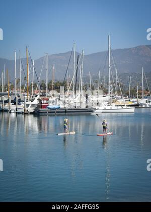 Deux femmes leur meilleur manœuvrier stand up paddle boards dans un canal près de voiliers et yachts amarrés dans la marina dans le port de Santa Barbara, Santa Banque D'Images