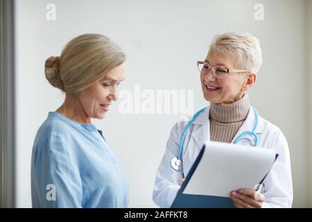 Waist up portrait of young female doctor smiling gaiement tout en parlant à senior woman prépare ses interventions médicales en clinique, copy space Banque D'Images