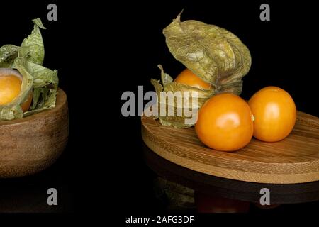 Groupe de quatre entiers et frais, de physalis orange bol bambou bambou ronde sur coaster isolé sur verre noir Banque D'Images