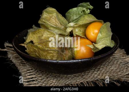 Beaucoup d'orange frais entier physalis avec tissu jute en vitrage isolé sur bol en verre noir Banque D'Images