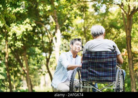 Les jeunes adultes asiatiques consolant fils père en fauteuil roulant à l'extérieur dans le parc Banque D'Images