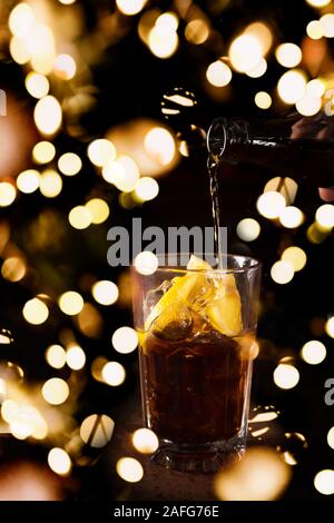 Barman prépare cocktail Cuba libre dans un grand verre sur le fond sombre. Shallow DOF avec lumières bokeh festive Banque D'Images
