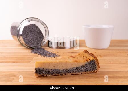 Un morceau de gâteau au fromage vegan aux graines de pavot avec une fourchette, une tasse de café et les graines de pavot sur une table en bois - vue oblique Banque D'Images