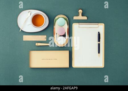 Mise à plat en milieu féminin. Bloc-notes, stylo, macarons et thé vert sur fond vert. Banque D'Images
