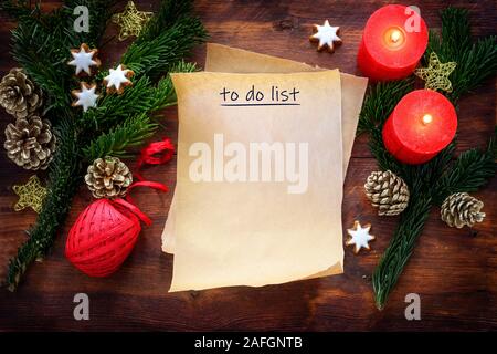 Feuille de papier avec du texte pour faire la liste sur la combustion rustique en bois sombre avec des bougies rouges, branches, la cannelle étoiles et décoration de Noël, copy space, haut Banque D'Images