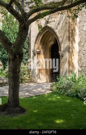 Jolie, ensoleillée, porte d'entrée de l'église à arc gothique à l'ombre tacheté de cerisier en été, église St Georges, Stamford, Lincolnshire, Angleterre, ROYAUME-UNI Banque D'Images