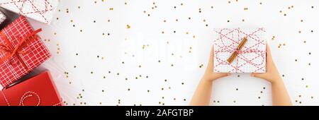 Bannière avec les mains de l'enfant holding gift box Cadeaux de fête, sur fond de bois blanc avec étoiles d'or de confettis. Mise à plat de style. Banque D'Images