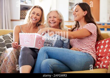 Mère avec sa fille adulte et Teenage Granddaughter Eating Popcorn Watching Movie at Home Banque D'Images