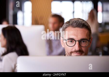 Homme de race blanche d'âge moyen à l'aide d'un ordinateur créatif dans un bureau occupé, portrait, Close up Banque D'Images