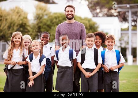 Portrait de plein air les élèves de l'élémentaire avec l'enseignant en uniforme debout sur terrain de jeu Banque D'Images