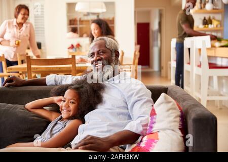 Grand-père avec sa petite-fille assis sur le canapé à la maison à regarder film avec la famille en arrière-plan Banque D'Images