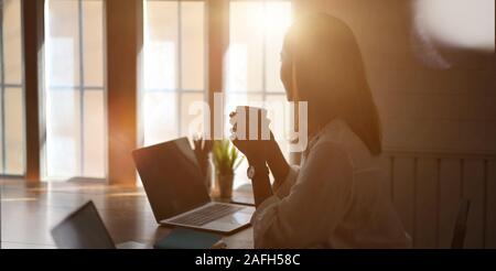 Cropped shot of young businesswoman working with laptop computer et de boire une tasse de café tout en regardant par les fenêtres Banque D'Images