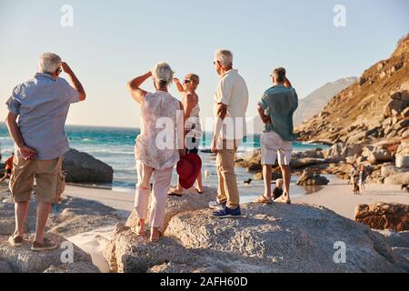 Vue arrière du Senior Friends Standing On Rocks Sur le groupe d'été surplombant la mer Banque D'Images